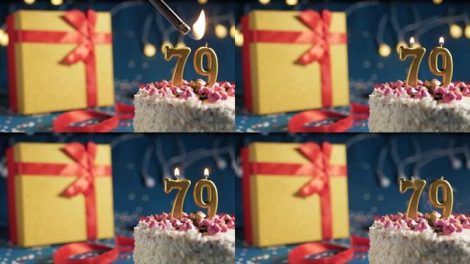 白色生日蛋糕79号点火器燃烧的金色蜡烛，蓝色背景带灯和用红丝带绑起来的礼物黄色盒子。特写