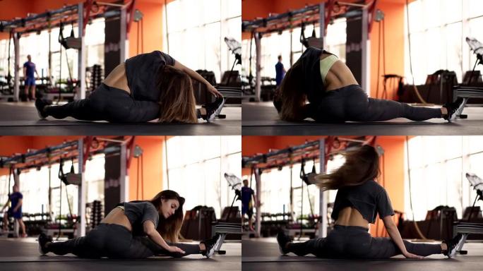 一个运动苗条的女人的肌肉背部的镜头，她练习健身并坐在现代的运动健身房中。她伸展双腿，积极地向腿弯曲。