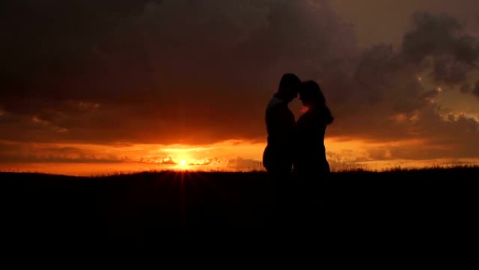 日落时分，一名孕妇和她的丈夫在田野里的剪影。