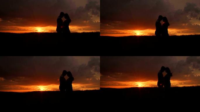 日落时分，一名孕妇和她的丈夫在田野里的剪影。