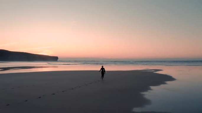 美丽的鸟瞰图迷人的冲浪女人在日落/日出时，带着她的冲浪板在沙滩上奔向大海。