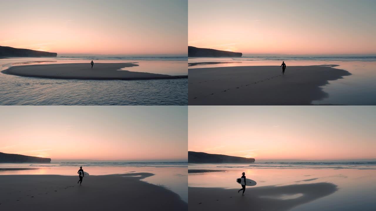 美丽的鸟瞰图迷人的冲浪女人在日落/日出时，带着她的冲浪板在沙滩上奔向大海。