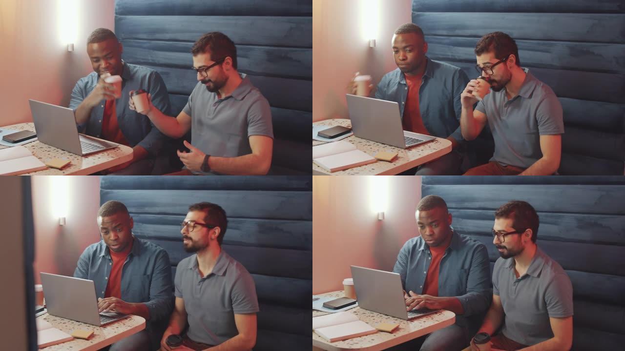 多元化的男性同事喝咖啡并在笔记本电脑上讨论项目