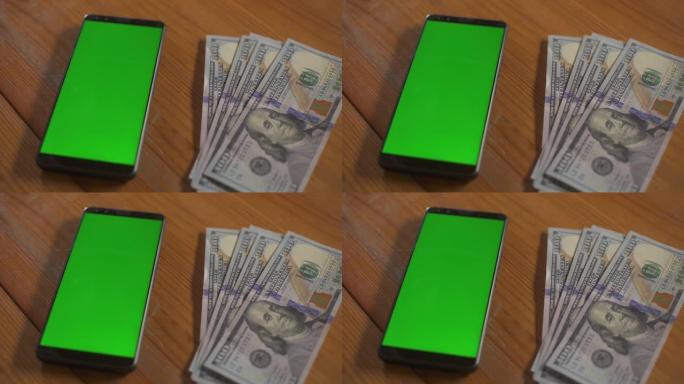 百美元钞票落在桌子上的手机屏幕触摸板旁边。绿屏手机模型。货币现金色度关键概念。技术和经济。个人预算。