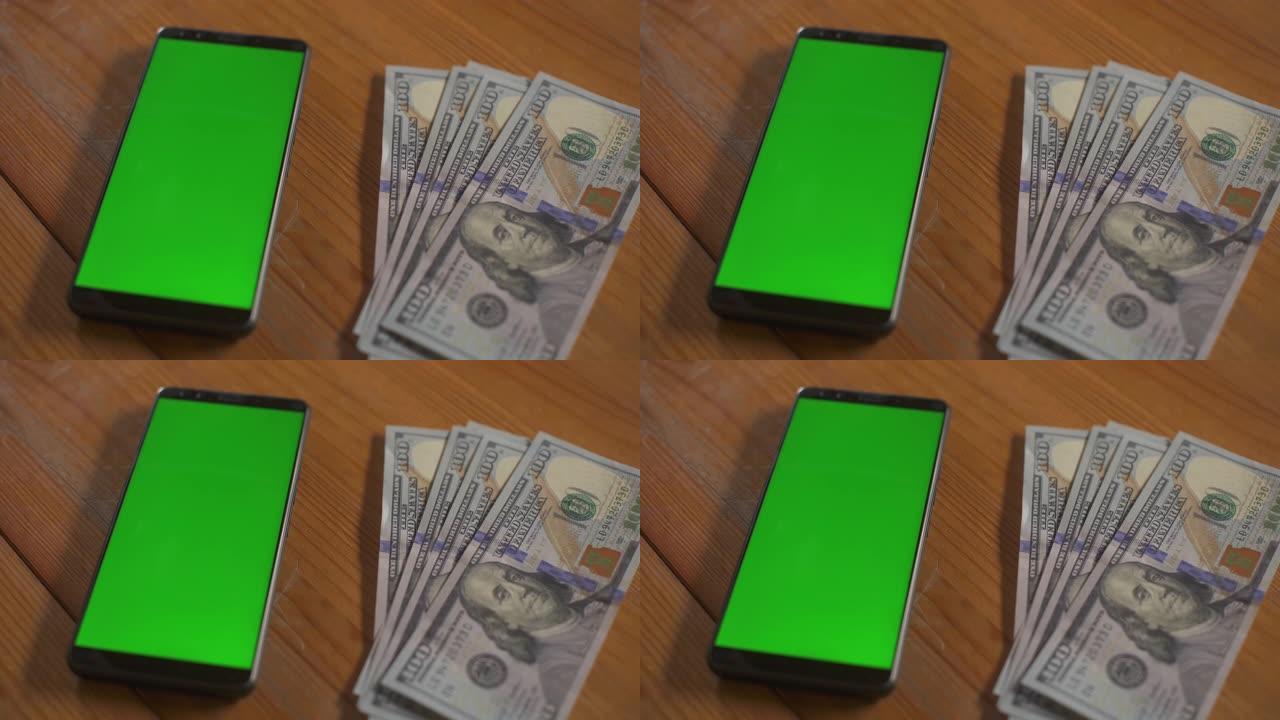 百美元钞票落在桌子上的手机屏幕触摸板旁边。绿屏手机模型。货币现金色度关键概念。技术和经济。个人预算。