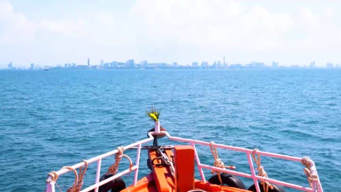 在热带自然的蓝天白云下，海面和芭堤雅市海岸线背景下运动的红色船首，风景优美。