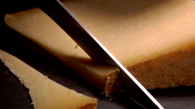 刀将硬奶酪切成薄片在黑色表面上