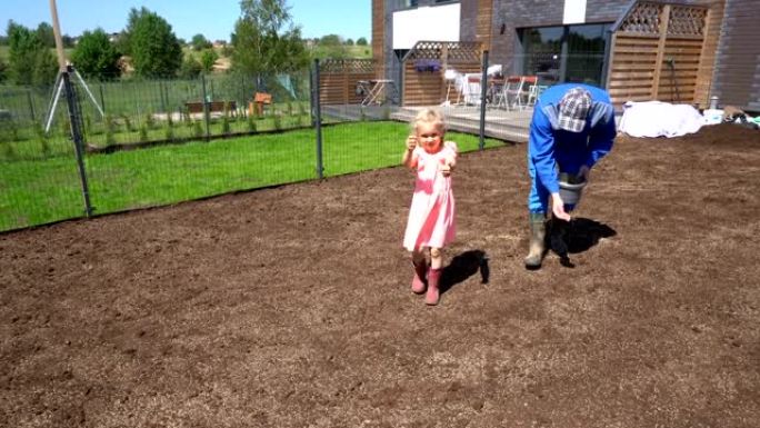 父亲和小帮手女儿在院子里播种草坪。手持镜头