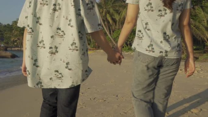 浪漫的亚洲年轻夫妇在海滩上牵着手，看着他们在日落时笑着，在蜜月时快乐。暑假和假期概念。
