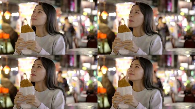 亚洲妇女在夜市享受鸡柳和街头美食