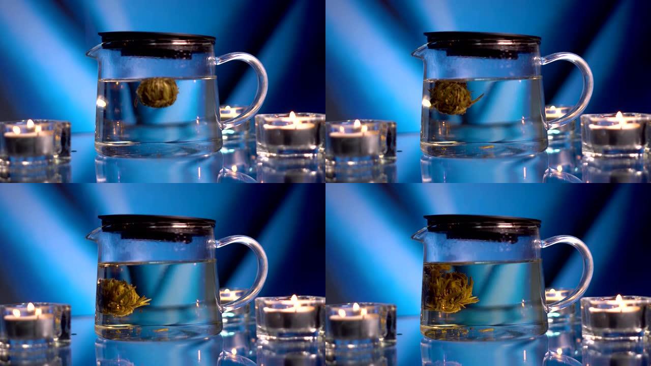 茶道。传统的中国花茶在昏暗的玻璃茶壶中盛开，在蓝色背景下，框架中有蜡烛。泡茶的奇妙过程