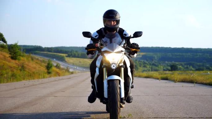 戴着头盔的人在高速公路上驾驶强大的运动摩托车，背景优美。骑摩托车的人沿着乡村道路用前灯驾驶摩托车超速