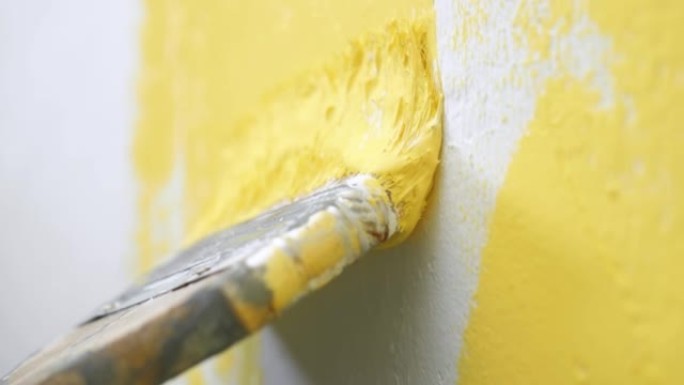 刷子在白色的墙壁上慢慢下降，并将其涂成黄色。壁画概念。慢动作和特写视图