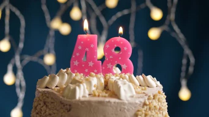 蓝色背景上有48号粉色蜡烛的生日蛋糕。蜡烛吹灭了。慢动作和特写视图