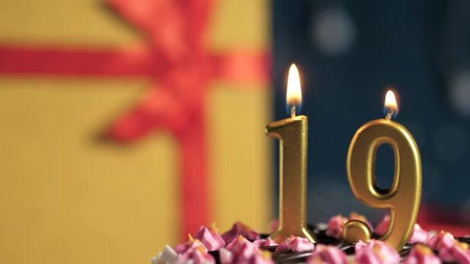生日蛋糕19号点火器燃烧的金色蜡烛，蓝色背景礼物黄色盒子用红丝带绑起来。特写和慢动作