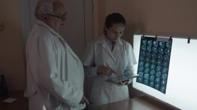 两名外科医生讨论头部的ct扫描和肩部的MRI扫描。神经外科医生团队在看病人的断层扫描时，讨论了他们将