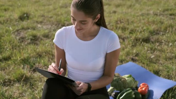 女孩坐在田野的草地上写作。