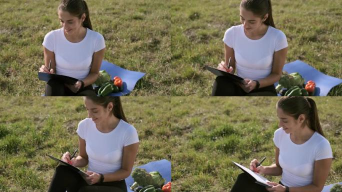 女孩坐在田野的草地上写作。
