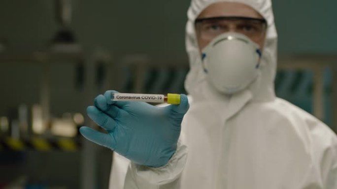 科学家拿着冠状病毒测试样品的试管。蒙面男实验室工作人员的肖像，研究人员在实验室里看着相机。冠状病毒2