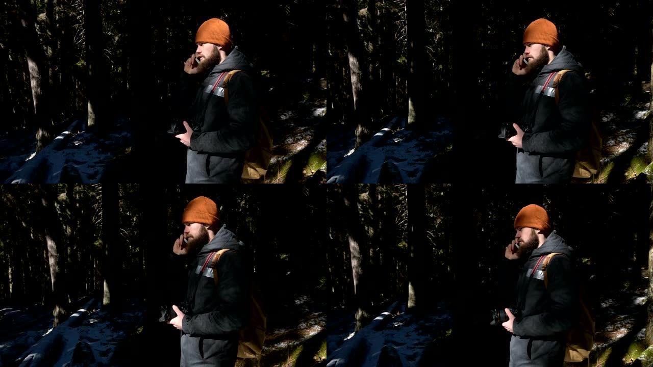 一个戴着帽子的大胡子男人在针叶林里用手机说话。难以到达的地方的蜂窝通信概念