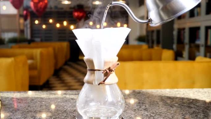 现代和另类的咖啡制作方式。咖啡师用咖啡机冲泡咖啡。双手合十，将热水倒入咖啡滤纸中。慢动作