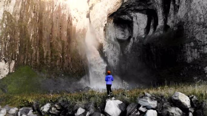 一个女孩是专业的风景摄影师，站在河边的石头上，拍摄大型史诗般的瀑布。鸟瞰图。北高加索
