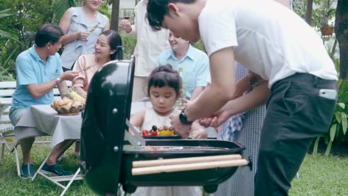 可爱的泰国女儿和她的姐姐和哥哥在户外花园为家人做烧烤派对