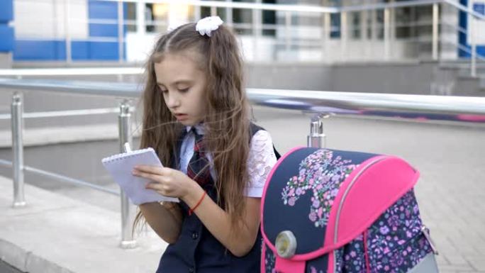 放学后在学校大楼附近穿着校服的女孩在笔记本上写东西。