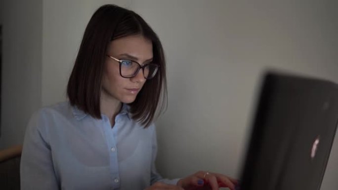 穿着衬衫和眼镜的女孩在笔记本电脑后面工作