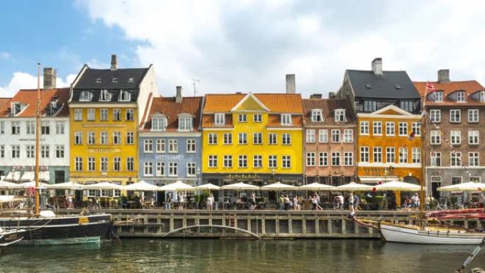 在丹麦哥本哈根Nyhavn市色彩缤纷的传统房屋中，人群在新鲜的日子里享受餐厅酒吧