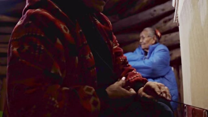 纳瓦霍族妇女在织布机上编织马鞍毯，她的母亲在背景中