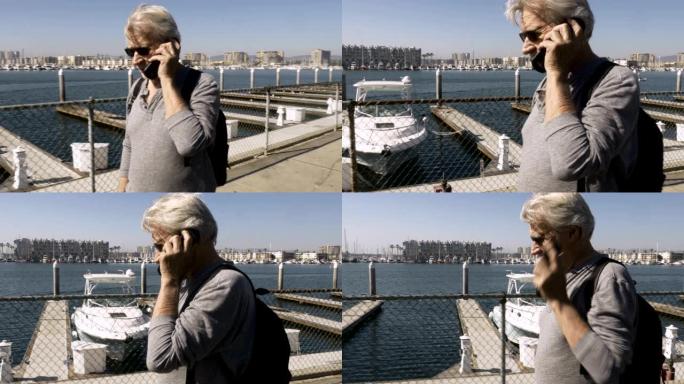 英俊的高级男子在翻盖电话上聊天，在码头散步