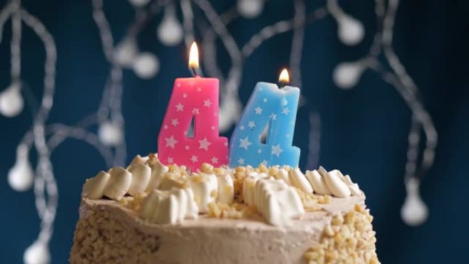 蓝色背景上有44号粉色蜡烛的生日蛋糕。蜡烛吹灭了。慢动作和特写视图
