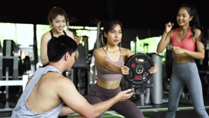 一群人为他们的亚洲女性朋友在健身馆用举重板下蹲而欢呼。作为团队合作一起工作。