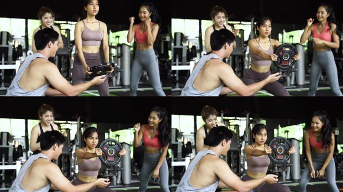 一群人为他们的亚洲女性朋友在健身馆用举重板下蹲而欢呼。作为团队合作一起工作。