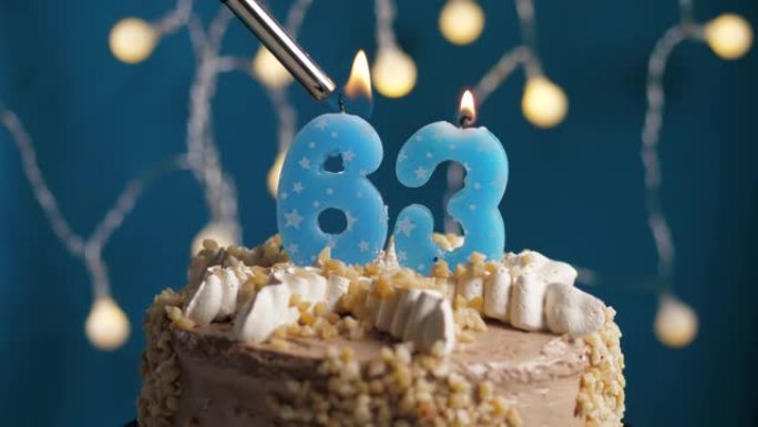蓝色背景上有63号蜡烛的生日蛋糕。蜡烛着火了。慢动作和特写视图