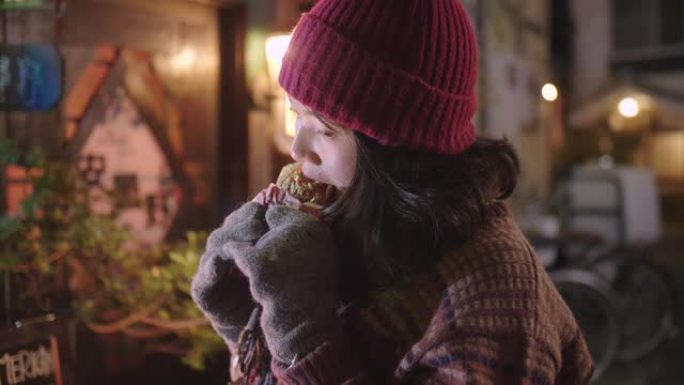 晚上在街上吃羊角面包Taiyaki (日本鱼形蛋糕) 的女人。