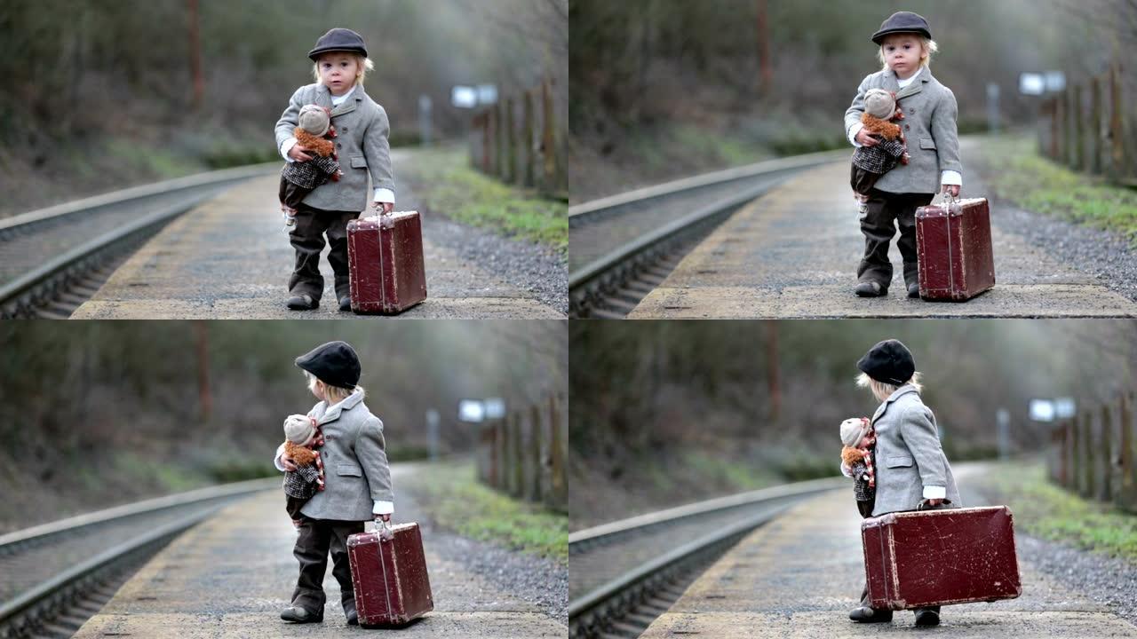 火车站上的可爱男孩，带着手提箱和漂亮的老式娃娃等着火车