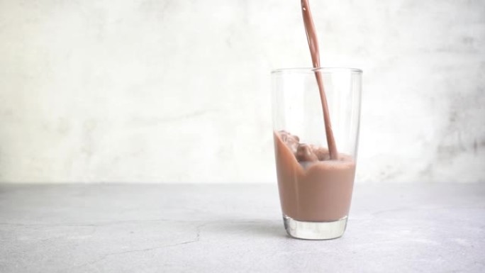 将巧克力牛奶加到桌子上的玻璃,慢动作。