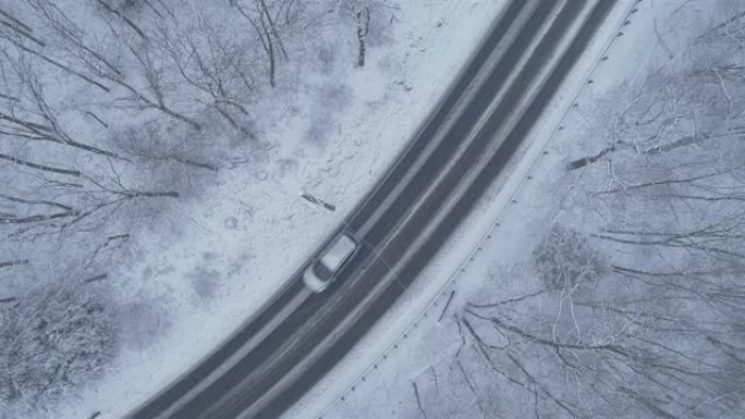 在降雪下驾驶高速公路穿过森林的汽车。无人机航拍视频与上升的摄像机运动。