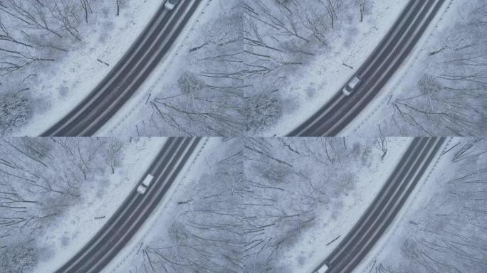 在降雪下驾驶高速公路穿过森林的汽车。无人机航拍视频与上升的摄像机运动。