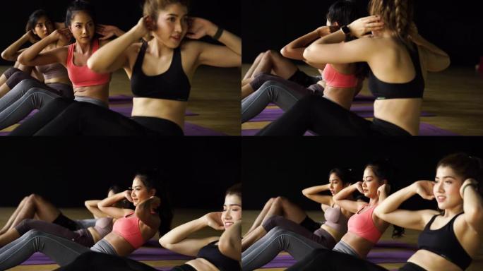 在有氧运动课上，亚洲男女在瑜伽垫上进行腹部锻炼。年轻的运动人士在健身房工作室的地板上扭动身体。