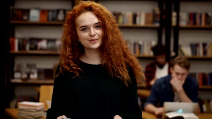 一个迷人的红发欧洲女学生站在高中图书馆微笑着看着相机微笑的肖像。教育、文学和人民观念。背景模糊的同学