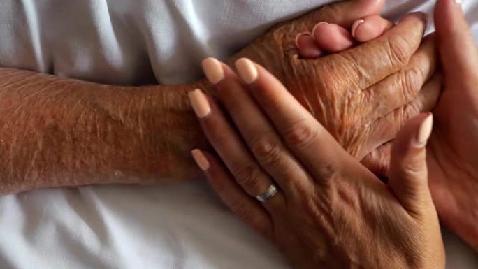女人拿着和温柔抚摸生病母亲的手给予支持。女儿安慰躺在医院床上的年迈妈妈皱巴巴的手臂。关心或爱的概念。