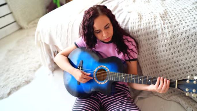 年轻女子在卧室弹吉他。年轻女子在床上弹吉他。她喜欢业余时间。美丽的女孩在舒适的卧室弹吉他