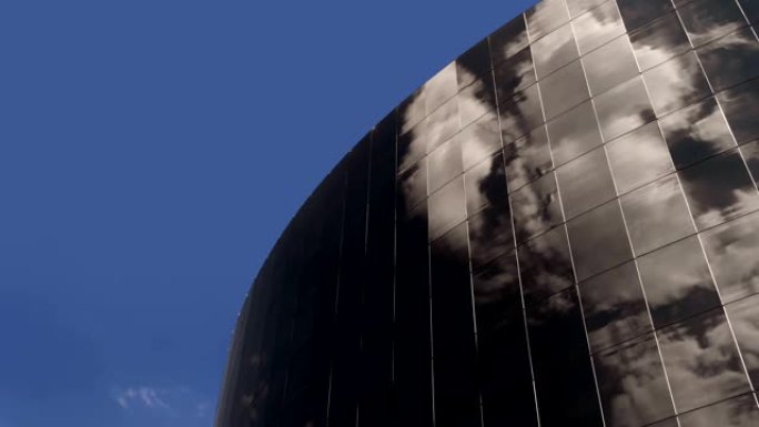 现代高层建筑的玻璃立面，其中反映了移动和旋转的云