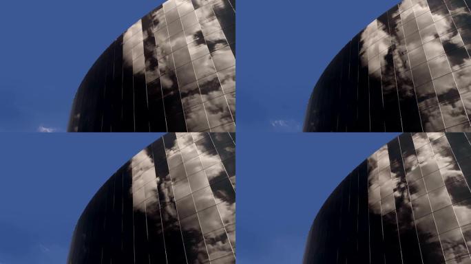 现代高层建筑的玻璃立面，其中反映了移动和旋转的云