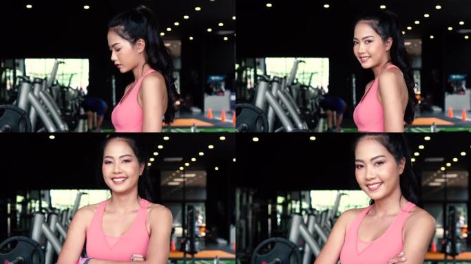微笑而坚定的年轻亚洲女运动员看着相机，双臂交叉并站在健身房健身中心