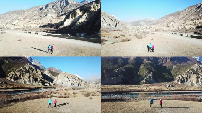 一对夫妇进入尼泊尔喜马拉雅山马南谷。他们正朝着干燥，尘土飞扬的道路上的一条小溪走去。他们周围的高山。