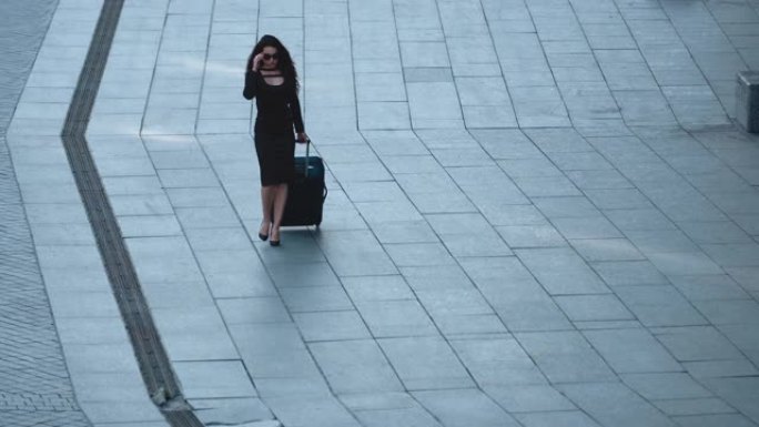 女人在街上带着行李行走。女人在街上看着手提箱